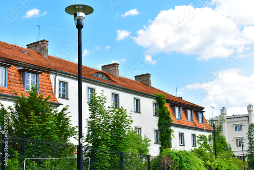 Rural house with white walls and red tiled roof in green trees on a sunny summer day with blue sky. Poland, Kurnik, Poznan, June 2022.