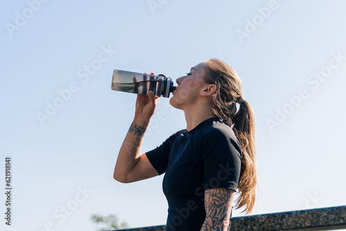 Fitness young sportswoman girl with tattoos doing sports in the morning drinking water while exercising outdoors in the city in the park health © Guys Who Shoot