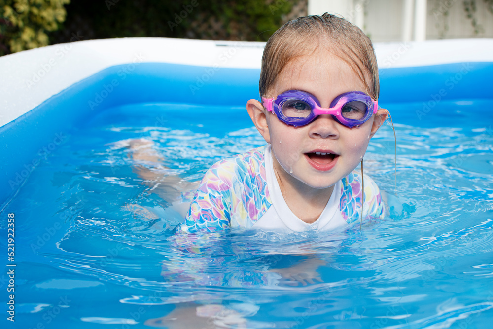 The Caucasian preschool girl is swimming in the inflatable pool in swimming goggles 