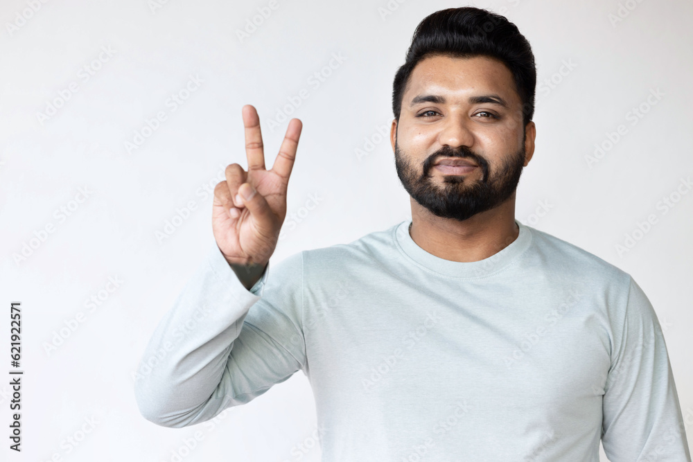 Confident Happy Smiling South Asian Man Pointing Up with V for Victory, two fingers Gesture for Success on Isolated Background Confident Happy Smiling South Asian Man Pointing Up with V for Victory, two fingers Gesture for Success on Isolated Background