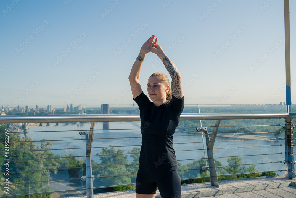 Fitness young sportswoman girl in the morning doing warm-up exercises before training on the street in the city on the bridge Sport health
