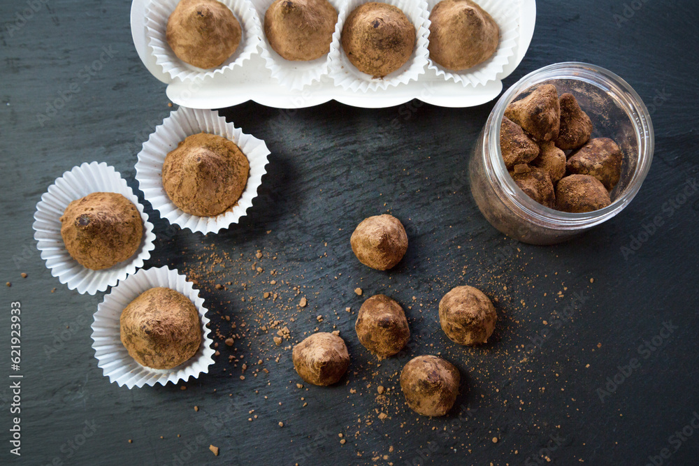 Fototapeta premium Truffle candies liberally sprinkled with cocoa white substrates on a black tray