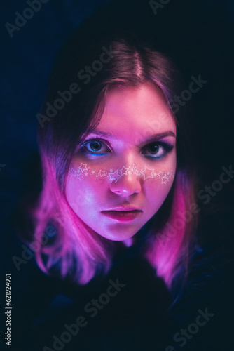 On a dark evening, a young and beautiful woman adorned with starry makeup radiates under a soft pink light. This portrait unveils themes of beauty, enchantment, and the allure of the night.  ©  Valeri Vatel