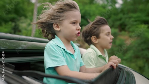 Adorable happy little boys children in open car sunroof during road trip, summer photo