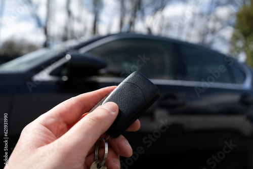 Fotografie Hand of man holding remote car key, next to a black vehicle.