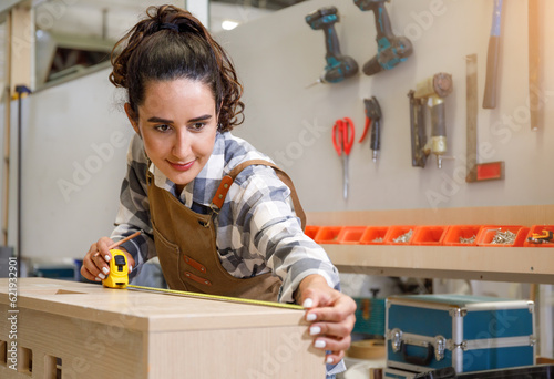 Young Latin female carpenter using a tape measure to measure dimensions to cut wood. to make furniture photo