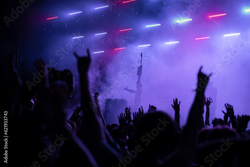 A group of people enjoy an illuminated music festival with raised arms. Concert Crowd in front of bright blue stage lights