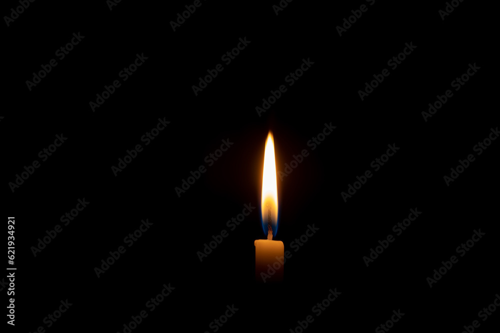 Single burning candle flame or light glowing on a small yellow candle on black or dark background on table in church for Christmas, funeral or memorial service with copy space. Single burning candle flame or light glowing on a small yellow candle on black or dark background on table in church for Christmas, funeral or memorial service with copy space.