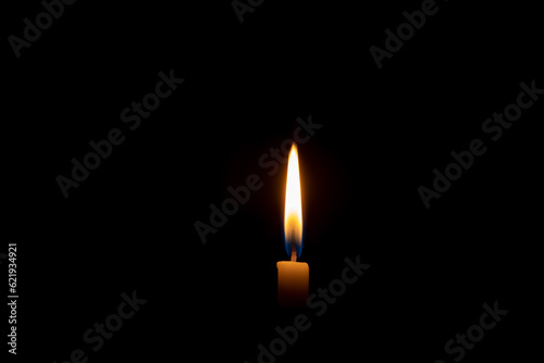 Single burning candle flame or light glowing on a small yellow candle on black or dark background on table in church for Christmas, funeral or memorial service with copy space.