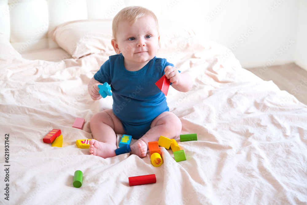 baby boy in blue bodysuit playing with colorful wooden eco toys on bed baby boy in blue bodysuit playing with colorful wooden eco toys on bed