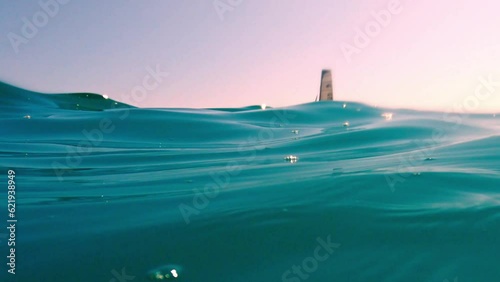 Extreme low-angle sea-level view of small sailboat sailing in calm open turquoise sea water with pink sky in background photo