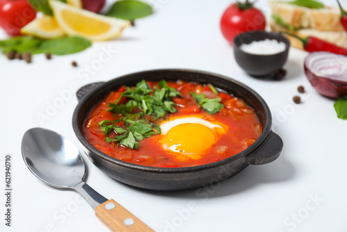 Shakshuka, spoon, slices of bread, tomato, lemon, basil, onion and spices on white background, close up