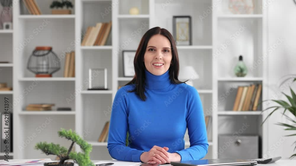 Portrait of young beautiful woman looking at camera and smiling. Adult stylish confident businesswoman sitting at workplace in bright office. Front portrait of modern successful female leader. Portrait of young beautiful woman looking at camera and smiling. Adult stylish confident businesswoman sitting at workplace in bright office. Front portrait of modern successful female leader.
