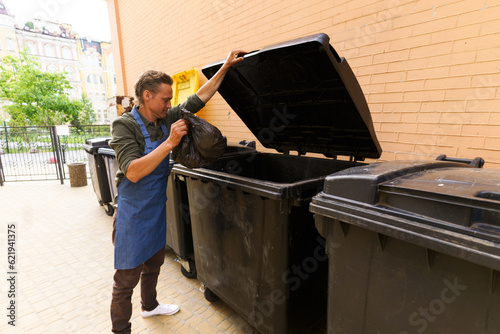Behang Waiter or kitchen worker responsibly disposing of garbage in pocket and placing it in city trash bin located in back yard
