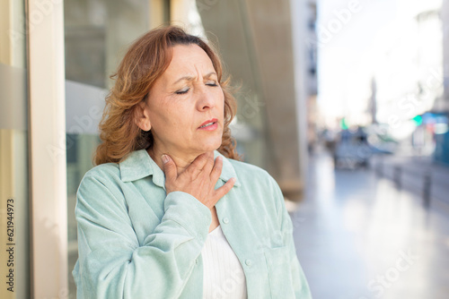 middle age woman feeling ill with a sore throat and flu symptoms, coughing with mouth covered