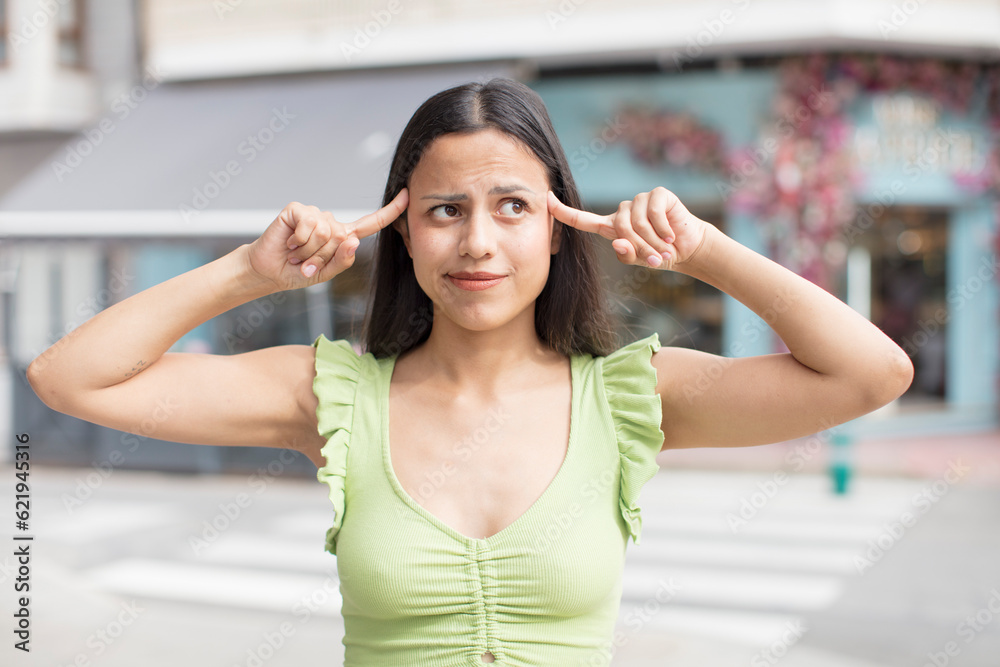 pretty hispanic woman feeling confused or doubting, concentrating on an idea, looking to copy space on side