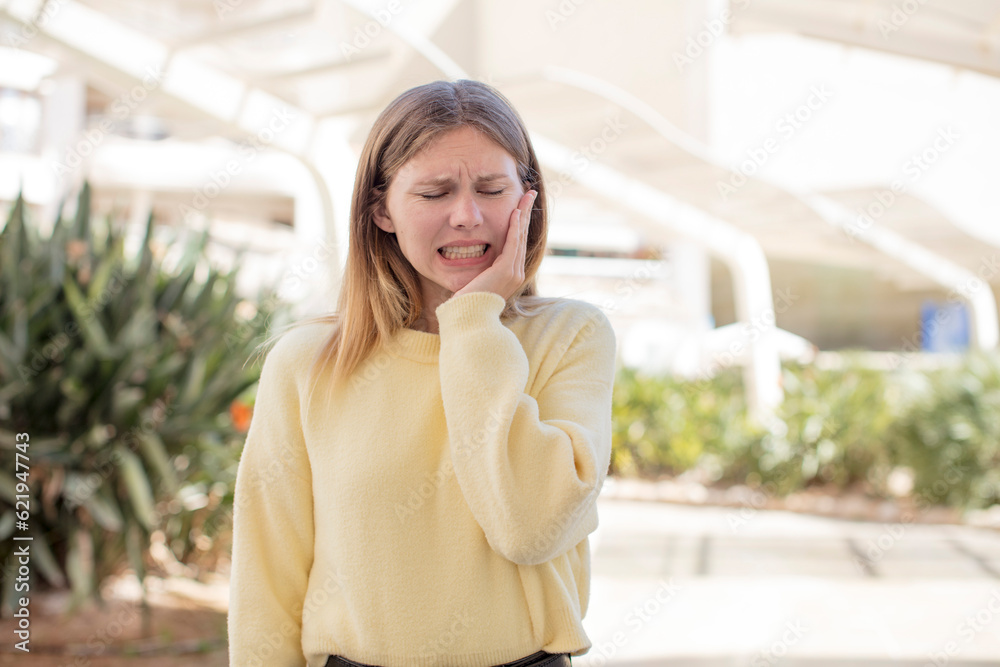 Fototapeta premium pretty young woman holding cheek and suffering painful toothache, feeling ill, miserable and unhappy, looking for a dentist