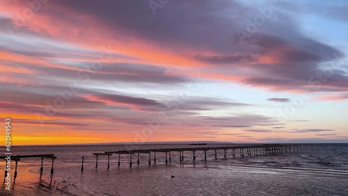 4K colourful view at sunrise of the old rotten pier with lenticular clouds moving along with calm waves in Punta Arenas, Patagonia, Chile photo