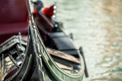 Fragment of a gondola, a Venetian boat on a blurred background of the canal water. Focus on the bow of the boat.