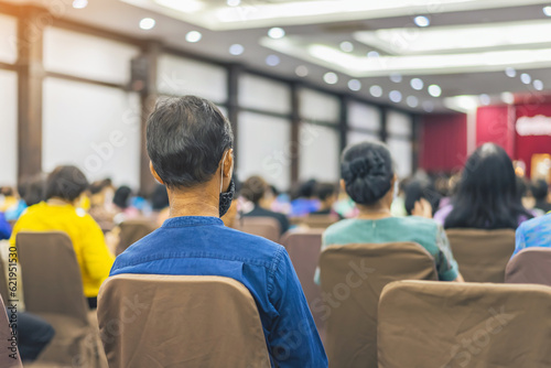 Back view of senior man wear face mask attending and listening to the annual meeting in the auditorium. Asian elderly active participants in conference room. Joyful listeners of business conference.