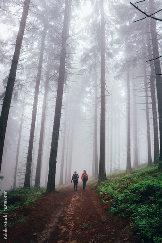 Two girls walk through a dark forest shrouded in a desolate grey mist on a rainy day. Horni Becva, Vsetinsko, Beskydy mountains photo