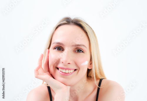 young blonde girl smiling with creams on her face leaning on her hand on white background