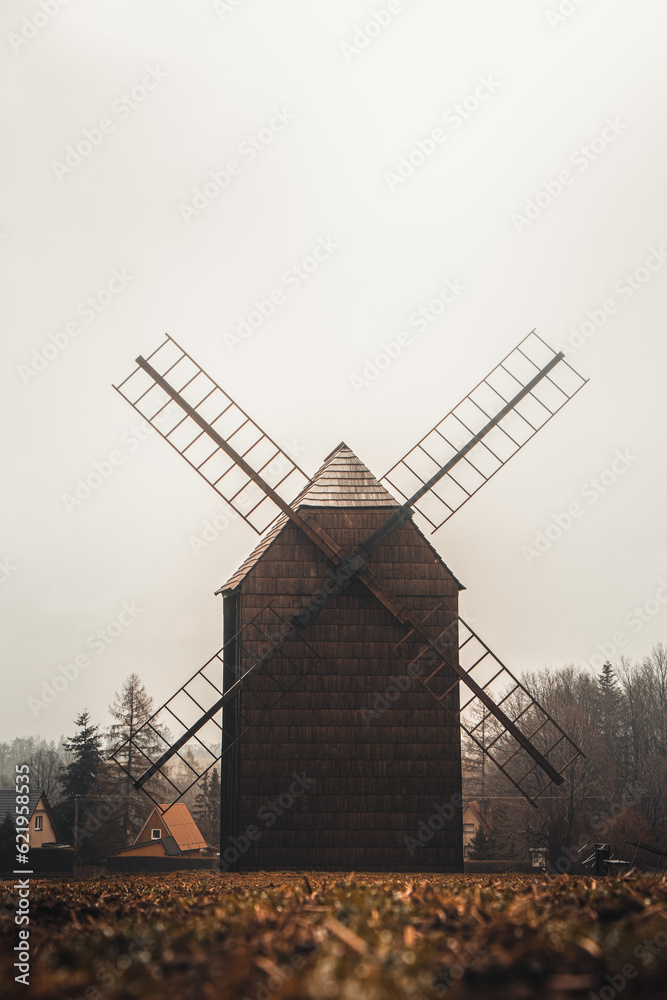 Ancient wooden mill standing alone in a field in gloomy foggy weather. Historical building for grinding corn, Opava, Czech Republic