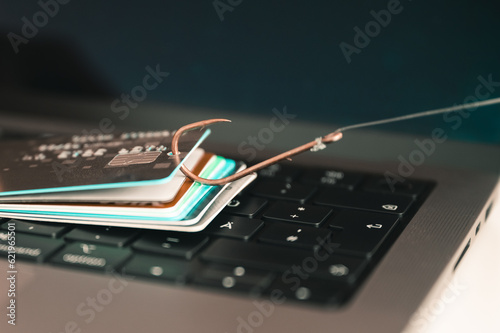 Visualisation of phishing and online fraud through a credit card hooked on a fishing hook by a data theft trying to obtain leaked credit card data for fraon a PC keyboard