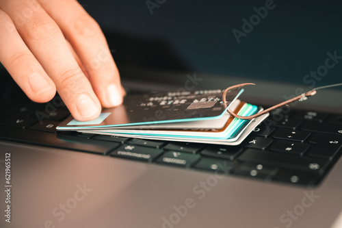 Visualisation of a person trying to prevent phishing and online fraud by holding a leaked credit card on a PC keyboard that is hanging on a fishhook photo