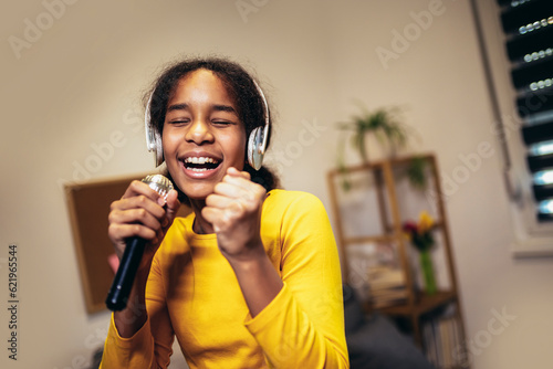 Cute preteen black girl holding a microphone singing karaoke at home, recording songs for a contest. Children's lifestyle concept