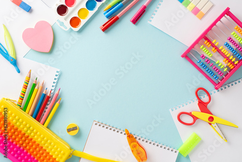 Embark on learning adventure with this top view composition: delightful collection of vibrant stationery set against pastel blue background, with round copyspace available for text or advertisements