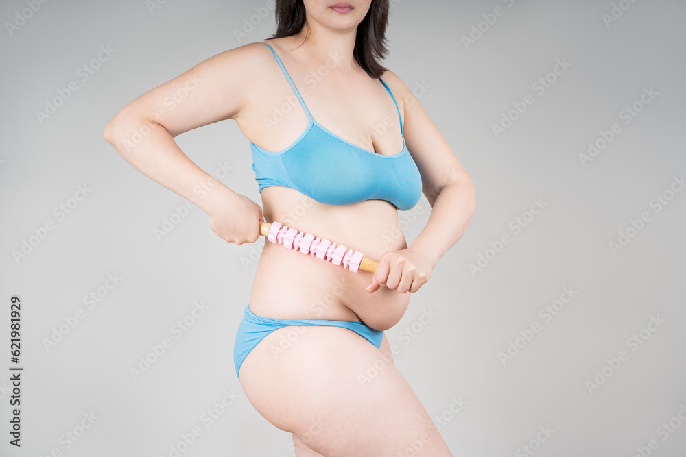 Fat woman with anti-cellulite roller massager on gray background Fat woman with anti-cellulite roller massager on gray background