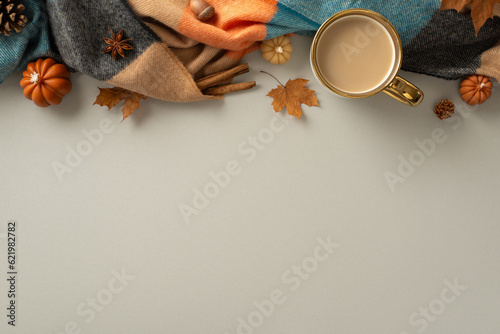 Above view of a warm and cozy autumn ambiance at home. Hot coffee, blanket, pumpkin candles, maple leaves and odorous cinnamon and badian create a perfect grey backdrop for text or advert placement photo