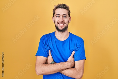 Hispanic man with beard standing over yellow background happy face smiling with crossed arms looking at the camera. positive person.