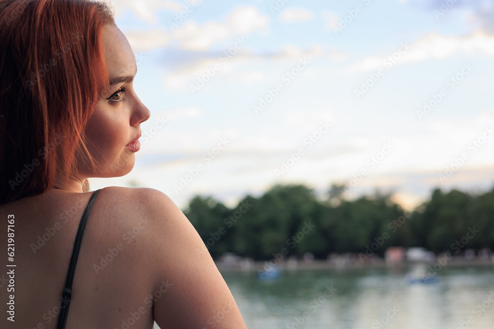 very beautiful freckled white woman with long red hair looking at the lake