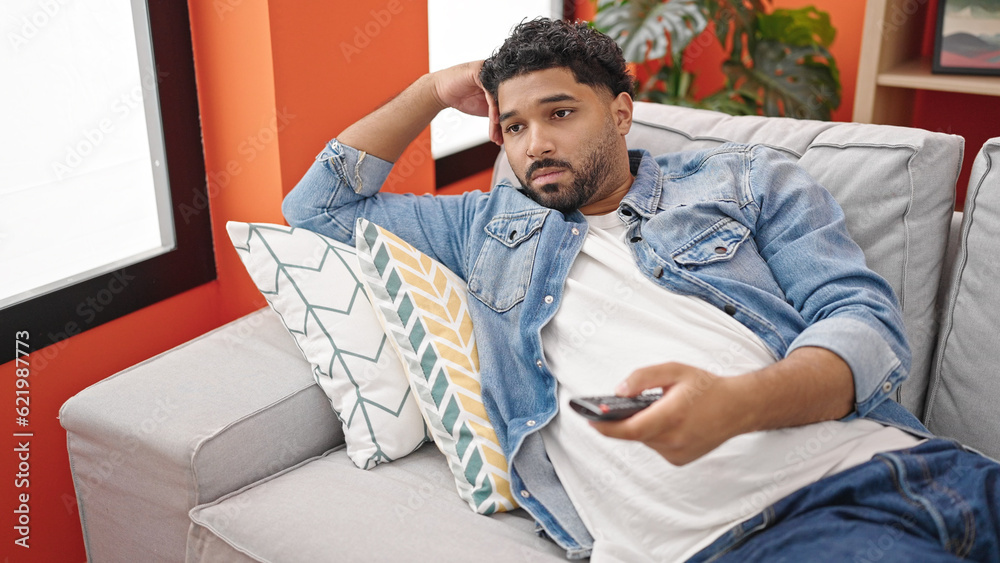 African american man watching tv lying on sofa with boring expression at home African american man watching tv lying on sofa with boring expression at home
