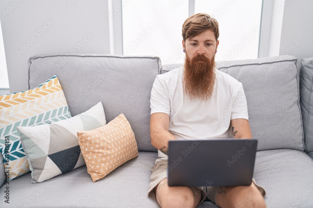 Young redhead man using touchpad sitting on sofa at home Young redhead man using touchpad sitting on sofa at home