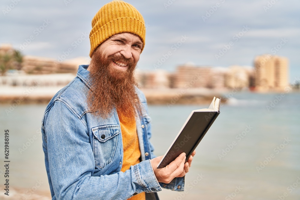 Young redhead man smiling confident reading book at seaside