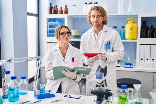 Two people working at scientist laboratory smiling looking to the side and staring away thinking.