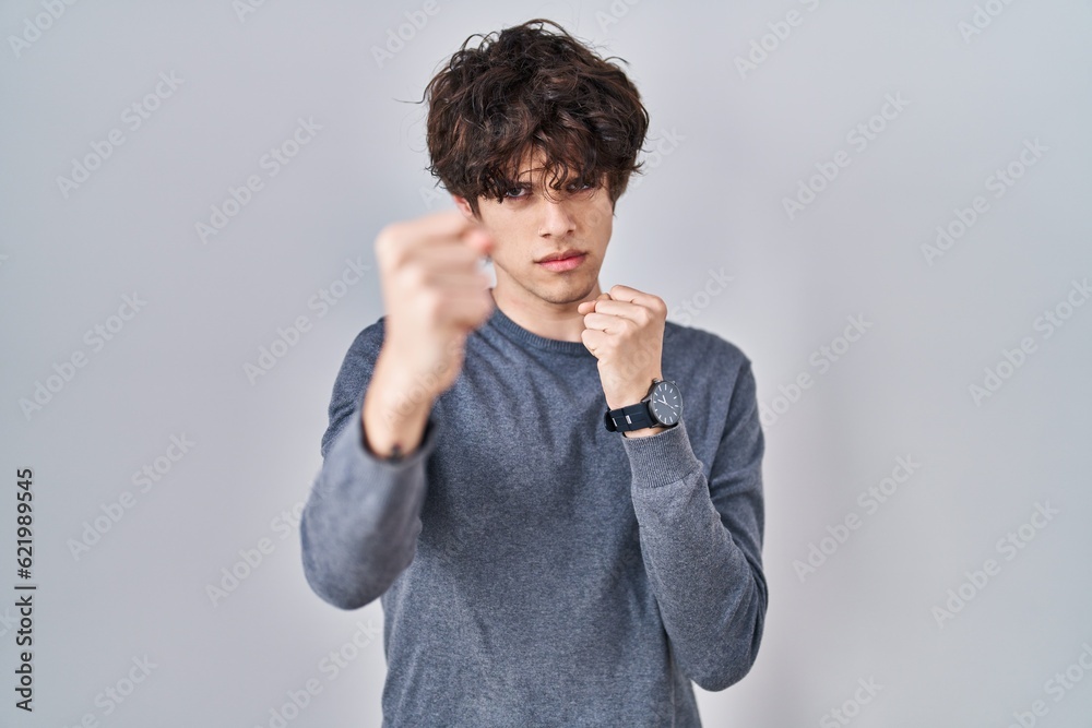 Young man standing over isolated background ready to fight with fist defense gesture, angry and upset face, afraid of problem Young man standing over isolated background ready to fight with fist defense gesture, angry and upset face, afraid of problem