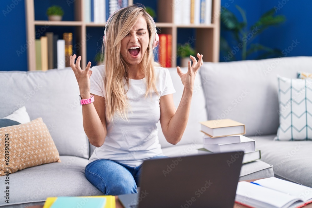 Young blonde woman studying using computer laptop at home crazy and mad shouting and yelling with aggressive expression and arms raised. frustration concept. Young blonde woman studying using computer laptop at home crazy and mad shouting and yelling with aggressive expression and arms raised. frustration concept.