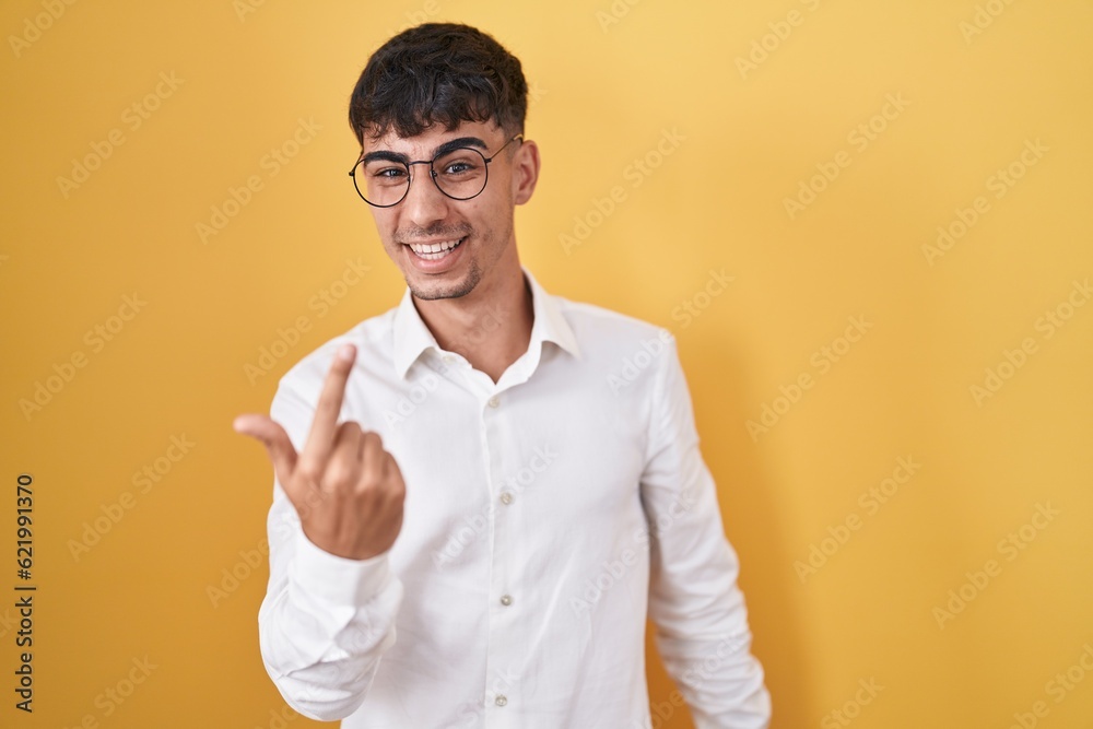 Young hispanic man standing over yellow background beckoning come here gesture with hand inviting welcoming happy and smiling Young hispanic man standing over yellow background beckoning come here gesture with hand inviting welcoming happy and smiling