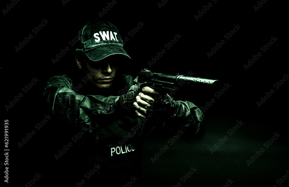 Spec ops police officer SWAT in black uniform aiming pistol with silencer, studio shot, half length