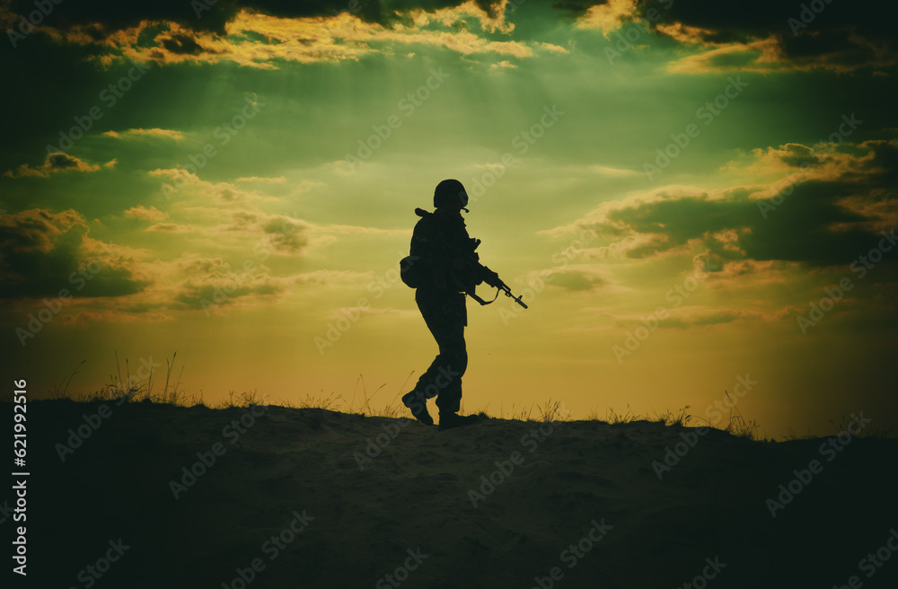Silhouette of US soldier with rifle at sunset standing as the sun sets in the background
