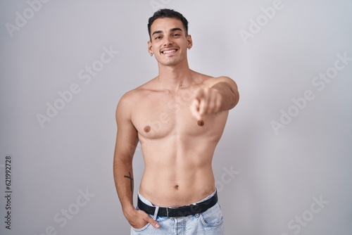 Handsome hispanic man standing shirtless pointing to you and the camera with fingers  smiling positive and cheerful