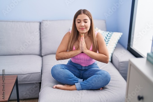 Young beautiful hispanic woman doing yoga exercise sitting on sofa at home