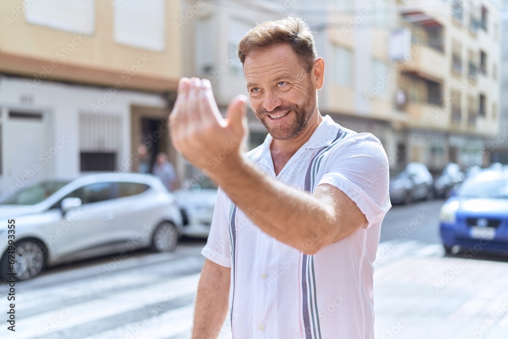 Middle age man smiling confident doing coming gesture with hand at street