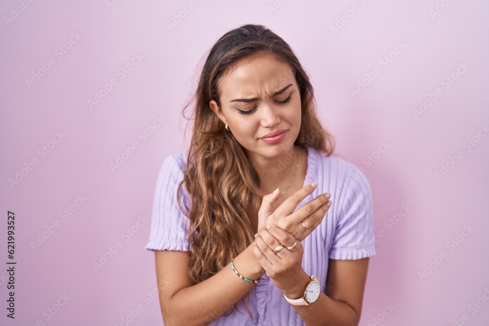 Young hispanic woman standing over pink background suffering pain on hands and fingers, arthritis inflammation Young hispanic woman standing over pink background suffering pain on hands and fingers, arthritis inflammation