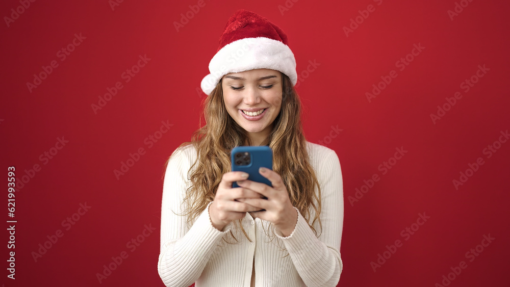 Young beautiful hispanic woman wearing christmas hat using smartphone over isolated red background Young beautiful hispanic woman wearing christmas hat using smartphone over isolated red background