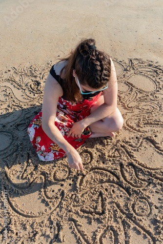 Woman Relaxes While Doodling in Beach Sand with Stick at Huntington Beach, California, USA, vertical